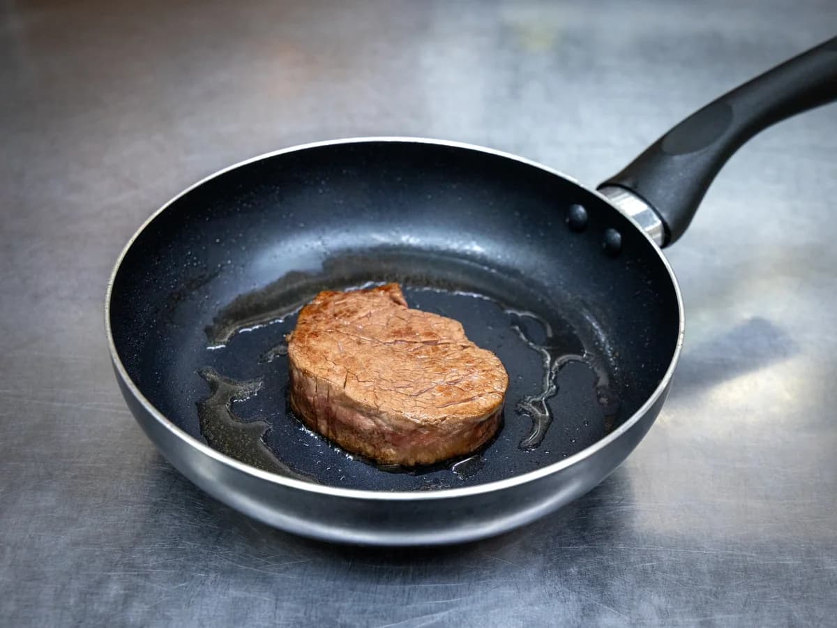 焼き目が十分につかないままフライパンで焼かれている肉